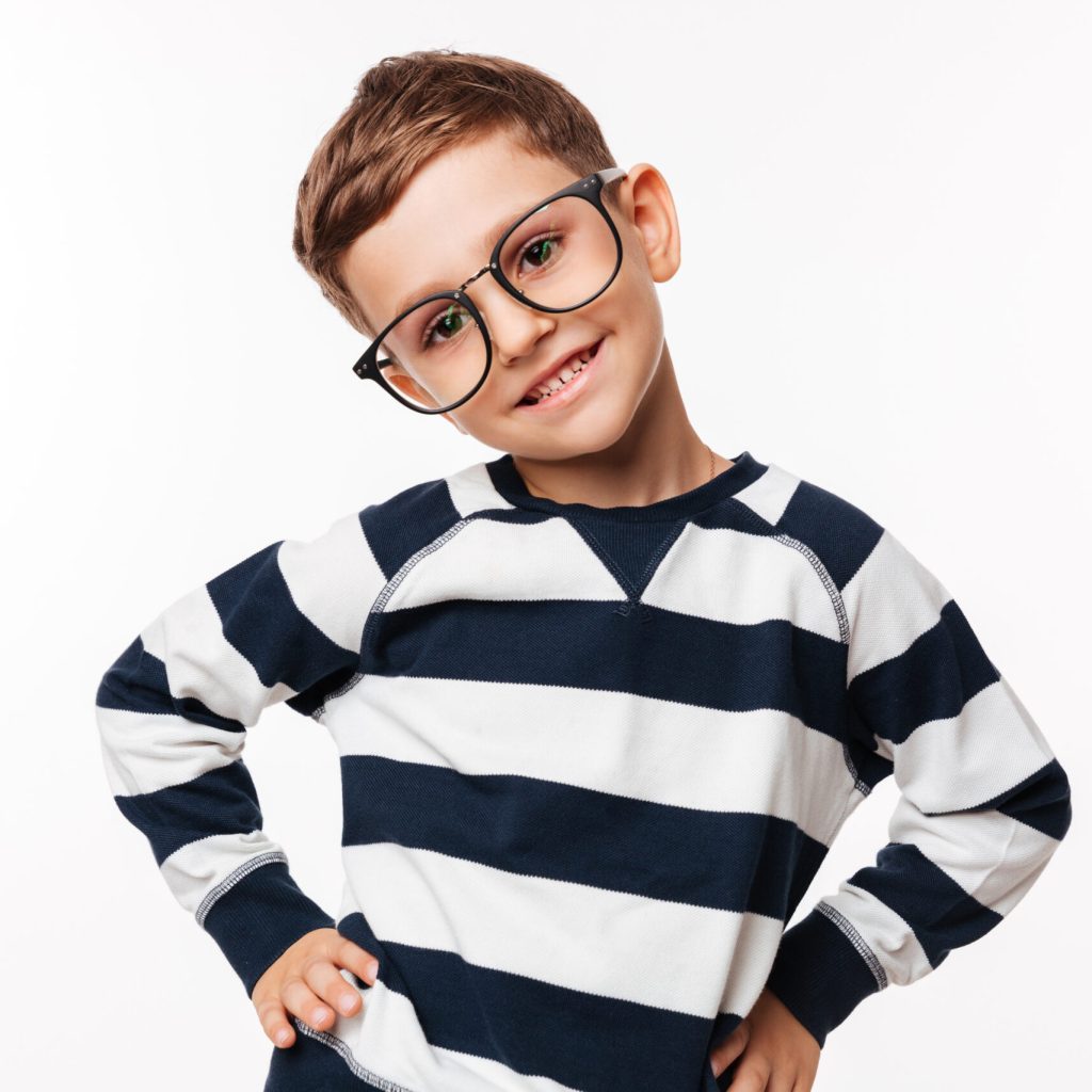 Portrait of a happy cute little kid in eyeglasses standing with arms on hips and looking at camera isolated over white background